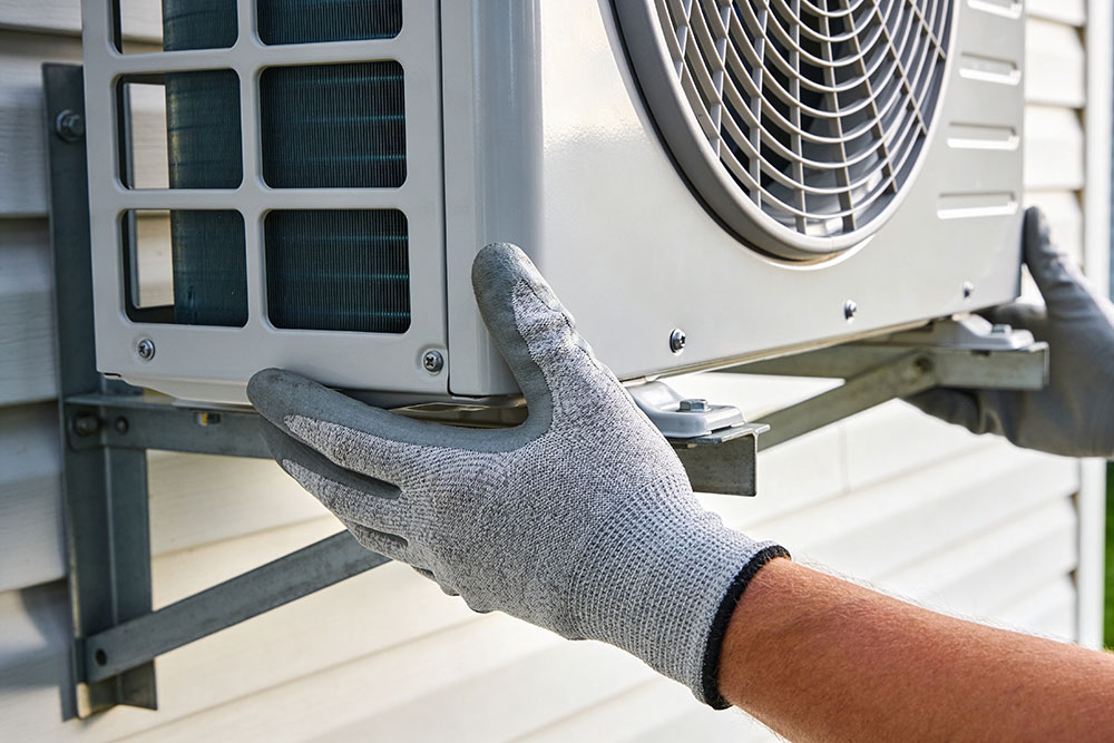 Technician installing outdoor HVAC unit with gloves, ensuring efficient air conditioning setup.