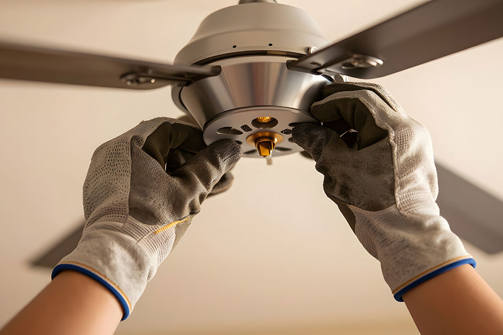 Hands installing a ceiling fan with gloves for safety and precision.