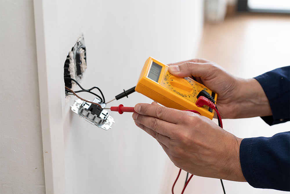 Electrician using a multimeter to test voltage in a wall outlet for safety and troubleshooting.