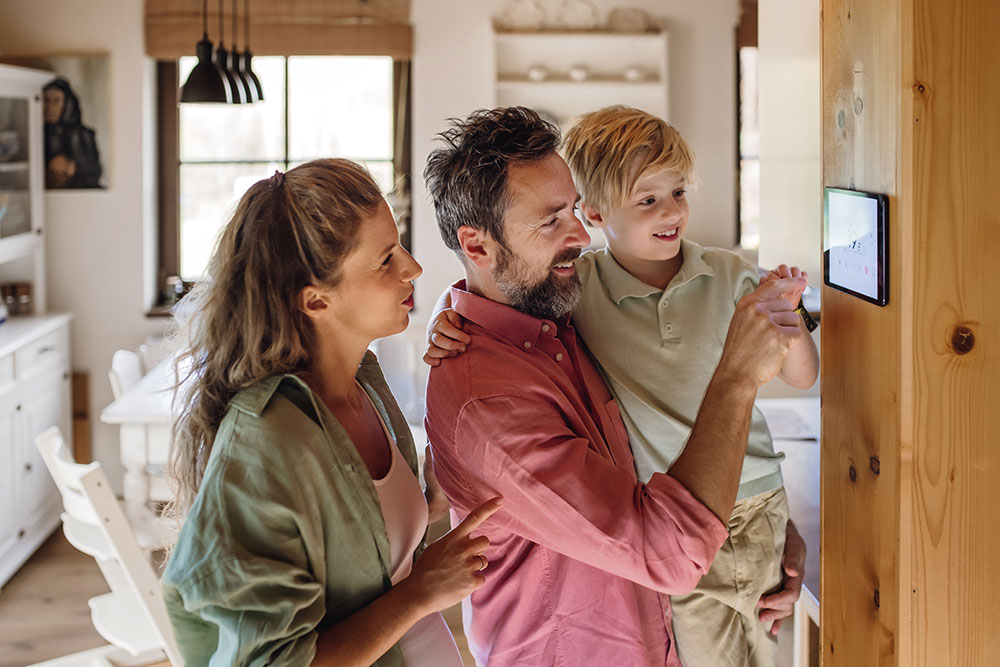 Family using smart thermostat on wall to control home temperature, emphasizing modern technology in cozy living space.