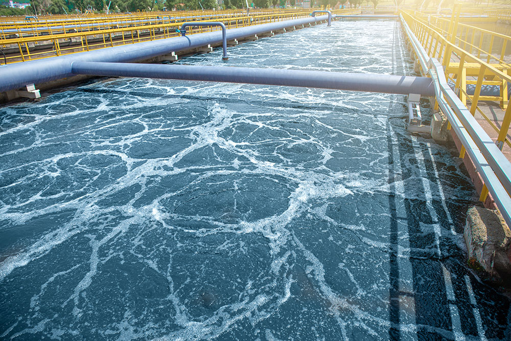 Aeration tank in a wastewater treatment plant with flowing water under sunlight, showcasing industrial water management.