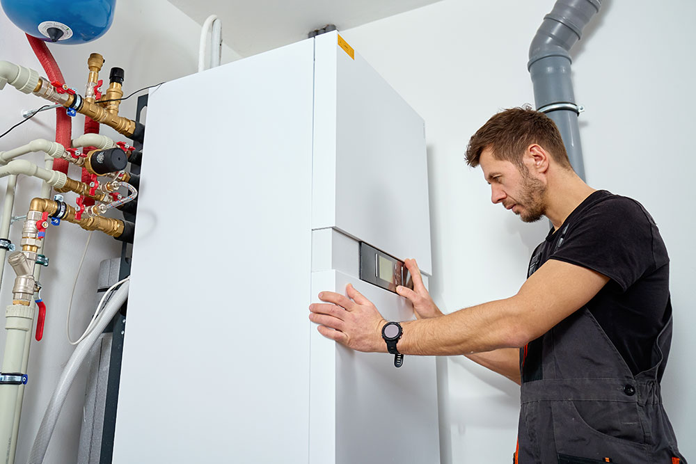 Technician inspecting modern water heater system with pipes in a utility room.
