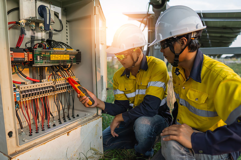 Technicians inspecting solar panel electrical wiring outdoors in safety gear, ensuring optimal energy efficiency.
