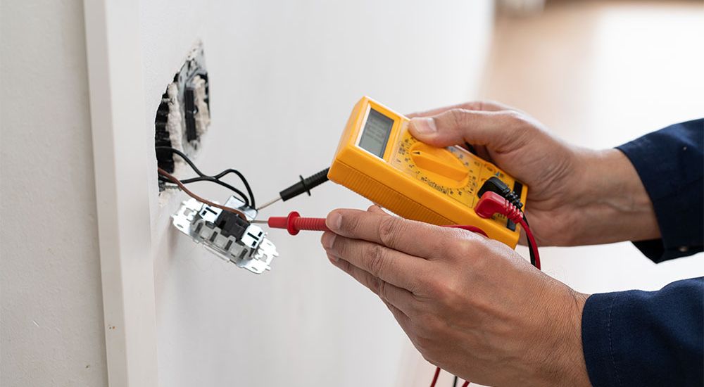 Electrician using a multimeter to test voltage in a wall outlet for safety and troubleshooting.