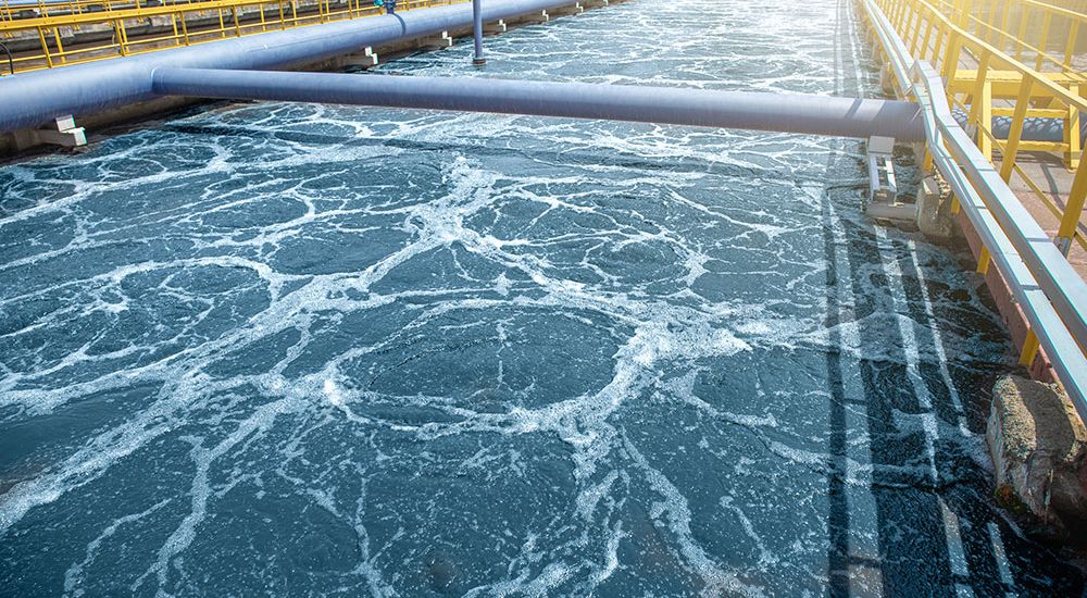 Aeration tank in a wastewater treatment plant with flowing water under sunlight, showcasing industrial water management.