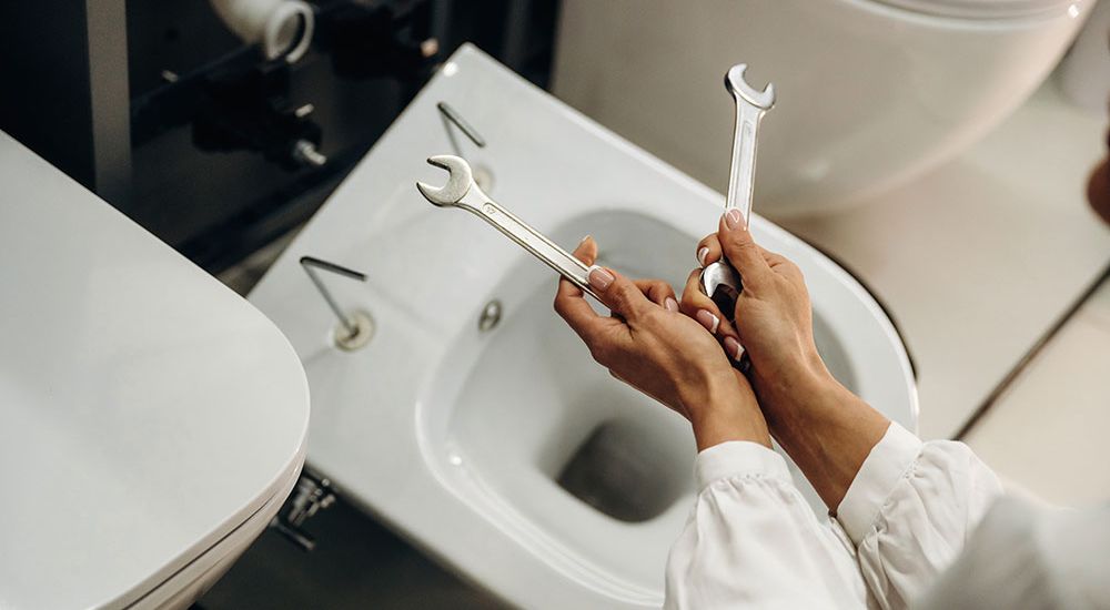 Person holding wrenches fixing a toilet; bathroom plumbing repair concept.