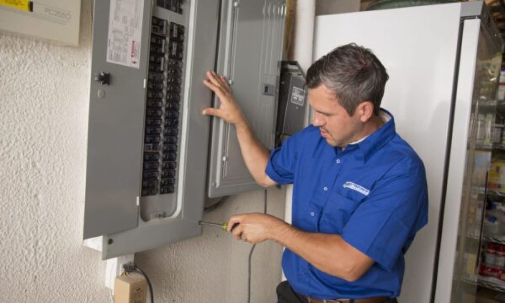 Technician in a blue shirt adjusting an electrical breaker panel on a wall