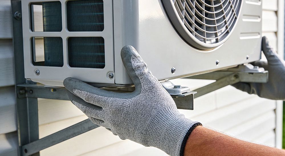 Technician installing outdoor HVAC unit with gloves, ensuring efficient air conditioning setup.