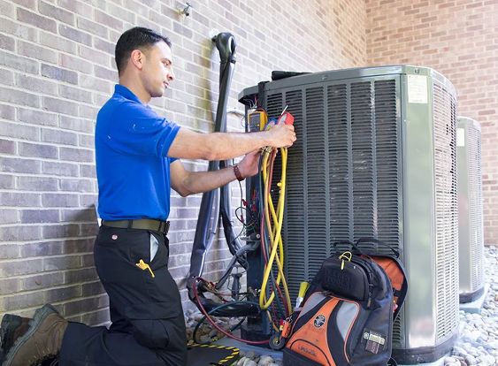 Technician servicing outdoor HVAC unit with tools outside brick building.