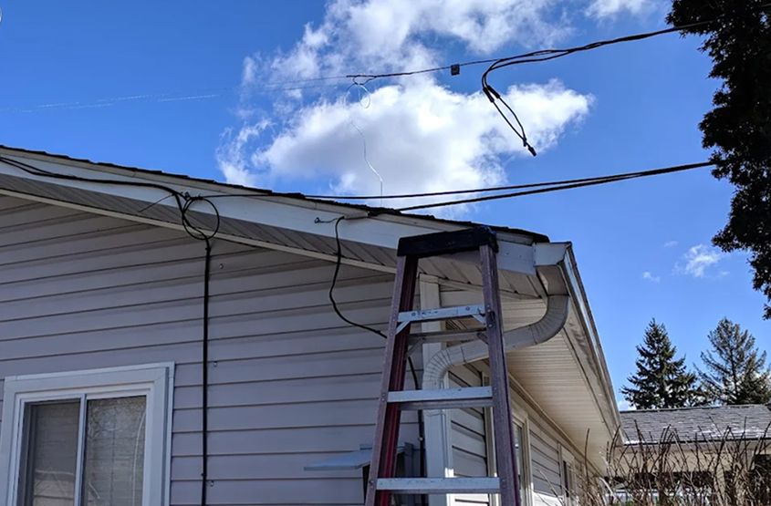 Ladder propped against a house with visible cables under a clear blue sky.