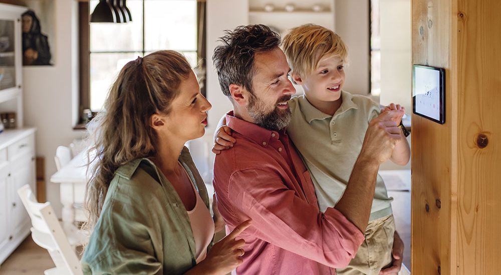 Family using smart thermostat on wall to control home temperature, emphasizing modern technology in cozy living space.