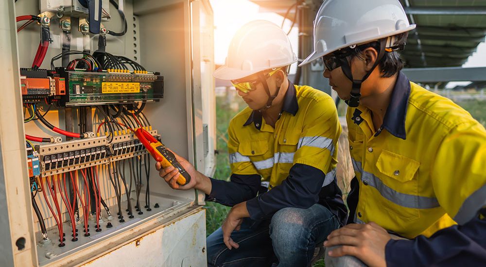 Technicians inspecting solar panel electrical wiring outdoors in safety gear, ensuring optimal energy efficiency.