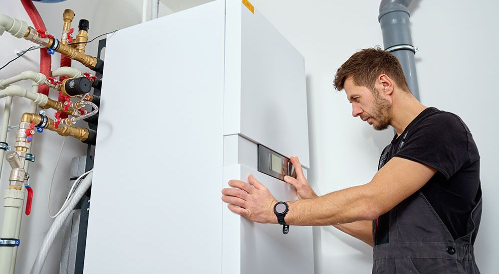 Technician inspecting modern water heater system with pipes in a utility room.