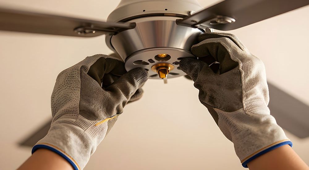 Hands installing a ceiling fan with gloves for safety and precision.